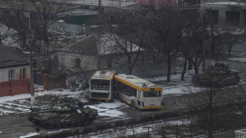 A tank moves down the street of a city in ruins.