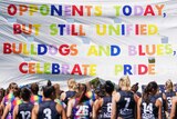 AFLW teams run through a banner reading "OPPONENTS TODAY BUT STILL UNIFIED. BULLDOGS AND BLUES, CELEBRATE PRIDE"