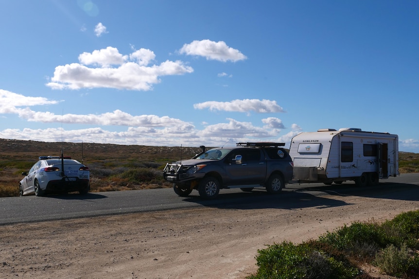 A four-wheel drive towing a caravan on a country road with a police vehicle parked in front of it.