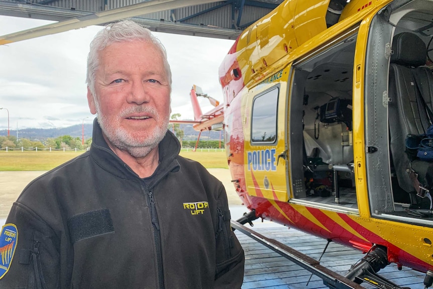 Rotor Lift Aviation Chief Pilot Peter McKenzie stands next to a rescue helicopter.