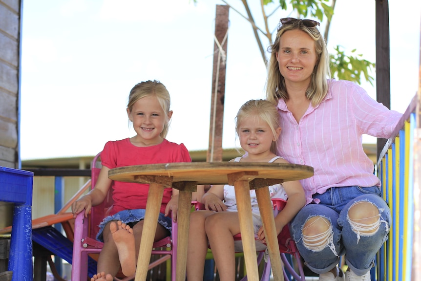 A mum smiles on a playground with her two young female children