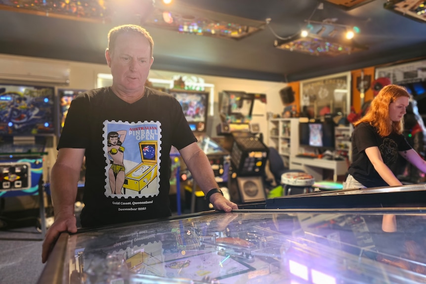 Doctor John Cosson and his daughter Emily Cosson playing pinball side-by-side in their Gold Coast home.