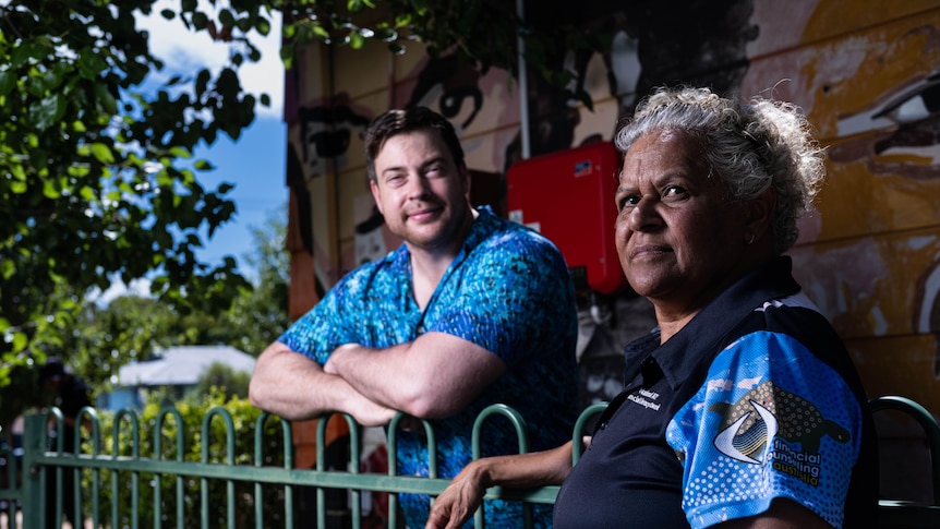 An Aboriginal man and woman stand next to a fence