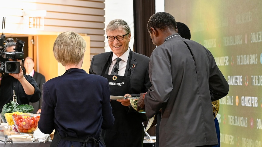 Bill Gates facing the camera, in conversation with a man and a woman with their backs to the camera