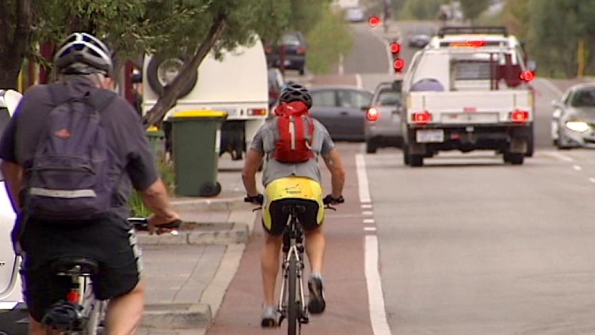 Two cyclists in a bike lane on a city road with traffic.