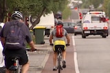 Two cyclists in a bike lane on a city road with traffic.