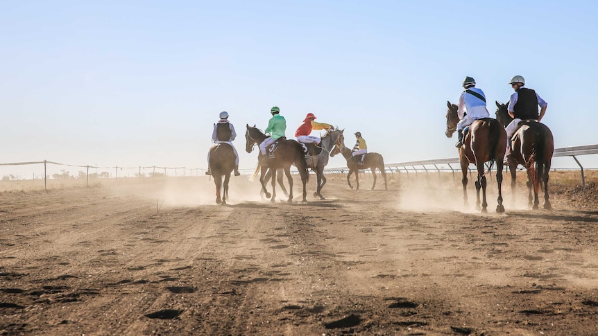 Six horses and jockeys on a dusty race track.
