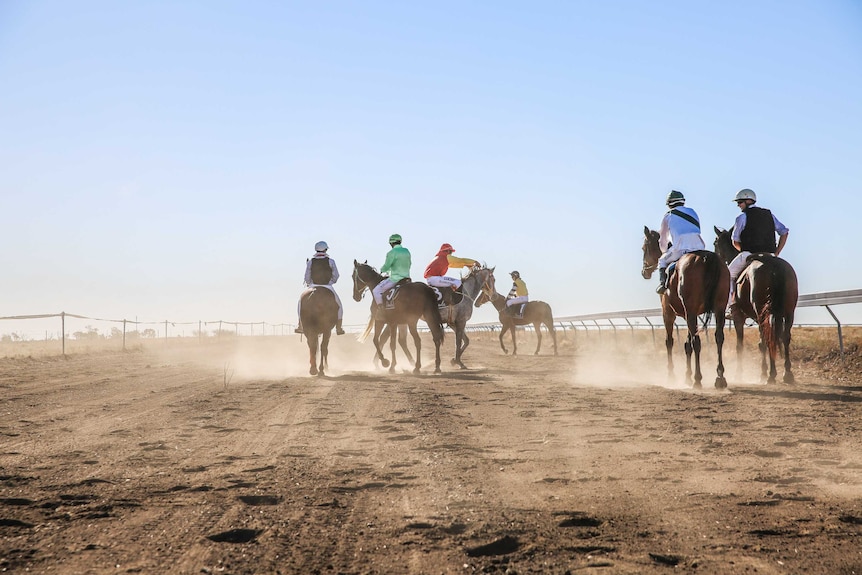 Six horses and jockeys on a dusty race track.