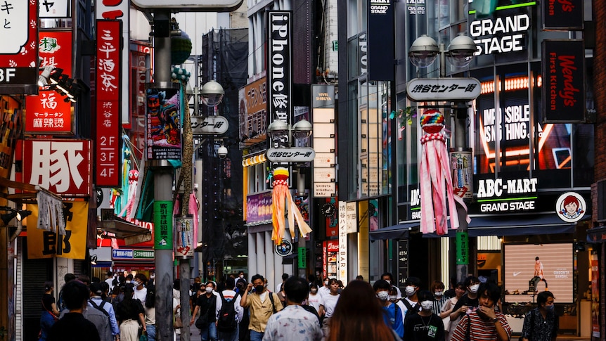 Crowds walk down a street in Japan covered in colourful billboards. 