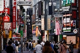 Crowds walk down a street in Japan covered in colourful billboards. 
