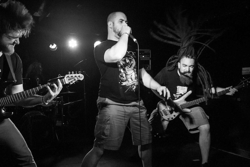 Black and white photo of three men performing on a stage in a metal band
