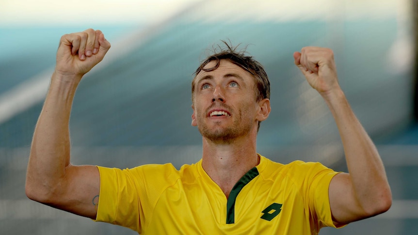 An Australian tennis player looks to the sky and raises his fists in triumph after a Davis Cup win.