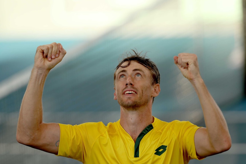 An Australian tennis player looks to the sky and raises his fists in triumph after a Davis Cup win.