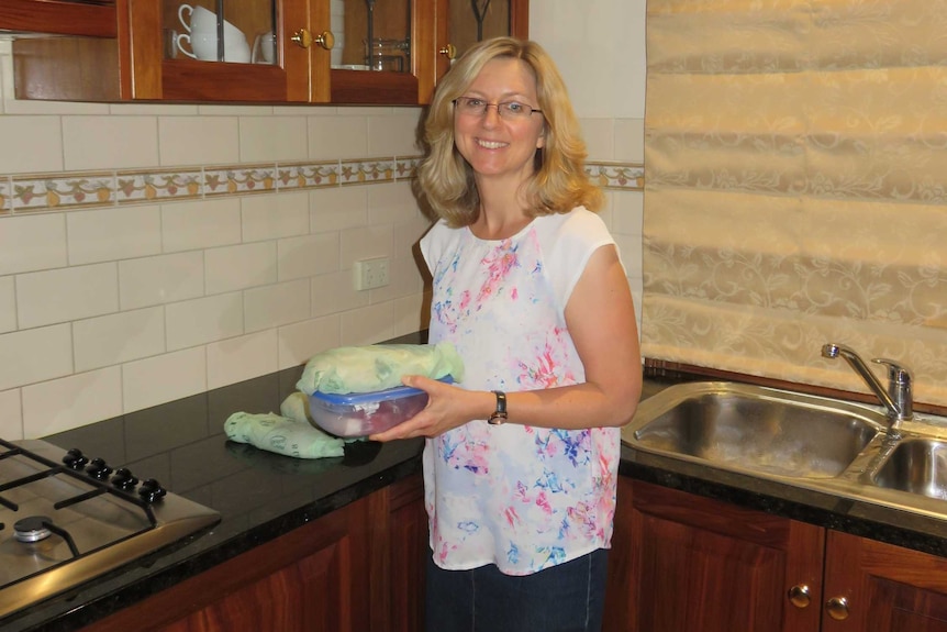 A woman stands in her kitchen showcasing food kept in reusable containers