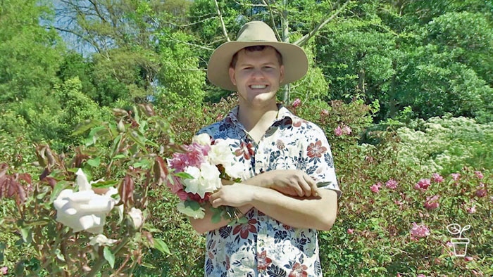 Man in hat standing in garden holding a bunch of roses