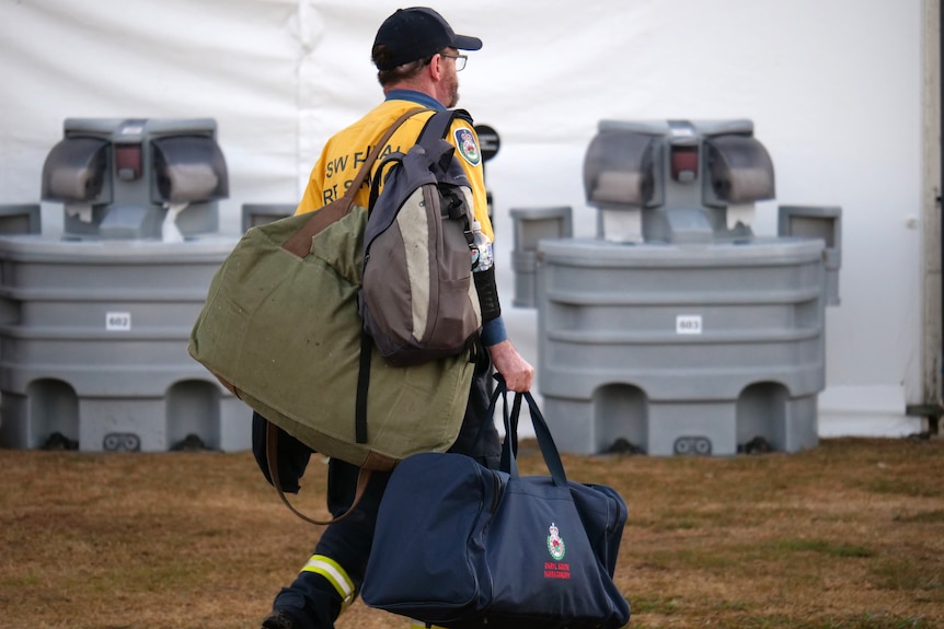 A man carries bags wearing a yellow firefighters uniform.