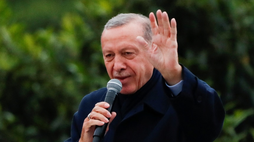 Turkish President Tayyip Erdogan holds a microphone waving at a crowd. 