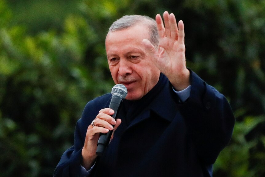 Turkish President Tayyip Erdogan holds a microphone waving at a crowd. 