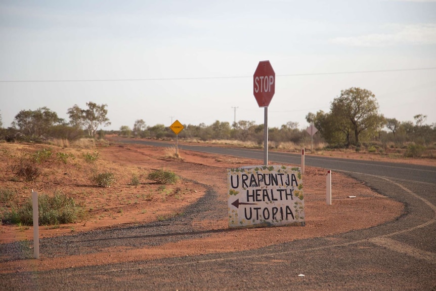A sign saying 'Urapuntja Health' sits against a stop sign at a turn off in Central Australia.