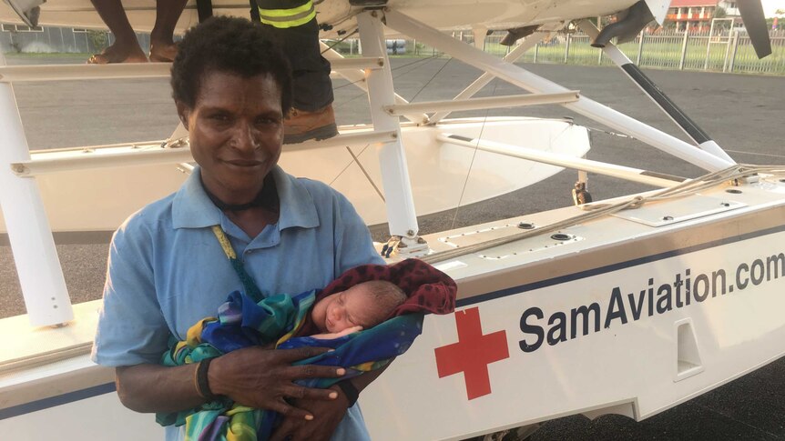 A woman holds a newborn next to Samaritan Aviation plane.