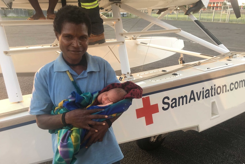 A woman holds a newborn next to Samaritan Aviation plane.