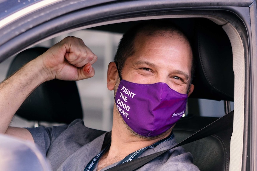 A man smiling with his fist up in a purple face mask reading 'Fight The Good Fight"