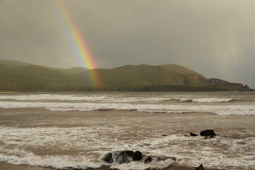 A rainbow shines into the water at a beach.