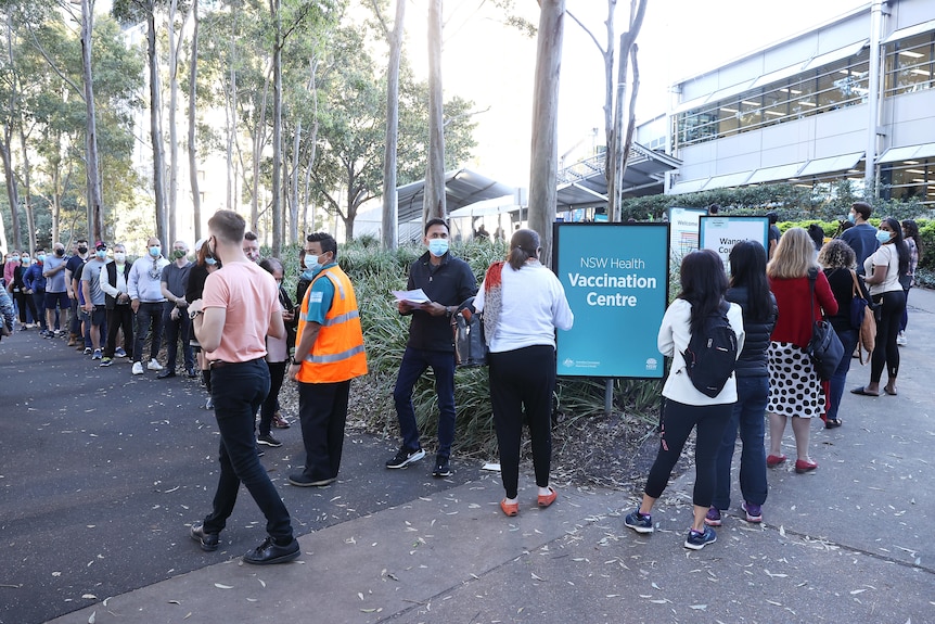 A long outdoor queue with marshals in orange vests