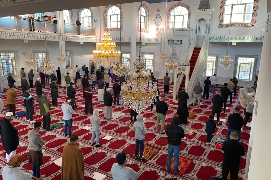 people socially distancing inside a mosque prayer rooms under chandeliers