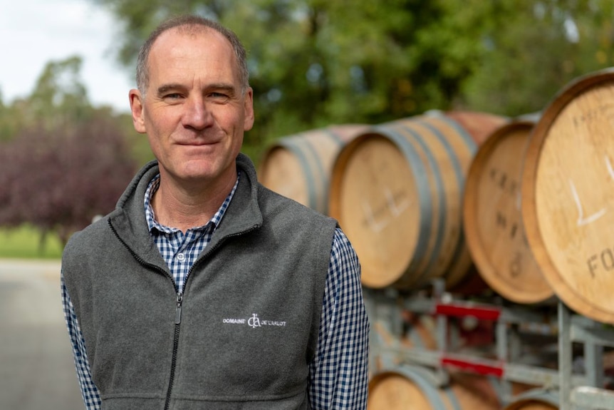 man stands in front of wine barrels