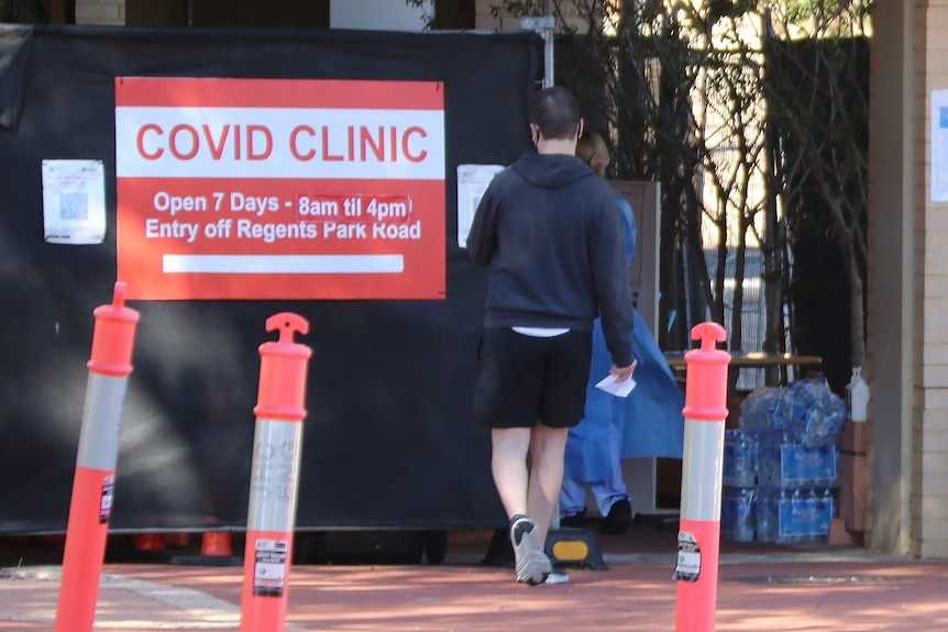 A man walks towards the entrance of a COVID-19 testing clinic with a big red and white sign on his left.
