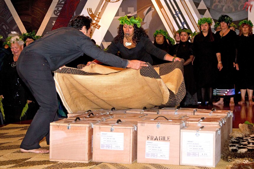 People cover small boxes containing Maori ancestral remains with a ceremonial cloak during a repatriation ceremony.