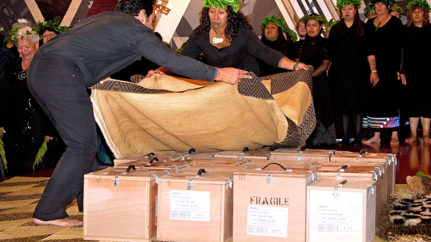 People cover small boxes containing Maori ancestral remains with a ceremonial cloak during a repatriation ceremony.