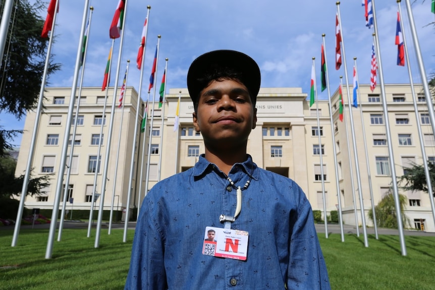 A photo of a young boy outside a building staring at the camera and smiling.