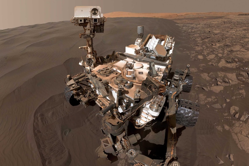 The Curiosity Rover takes a selfie at a dune of black sand.