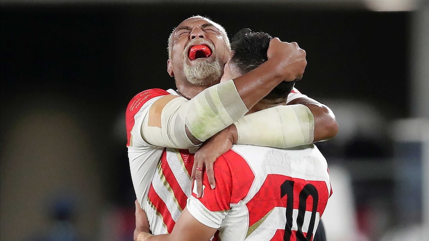 Japan's Isileli Nakajima is hugged by a teammate as he yells in joy, exposing a red mouthguard.