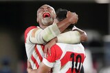 Japan's Isileli Nakajima is hugged by a teammate as he yells in joy, exposing a red mouthguard.