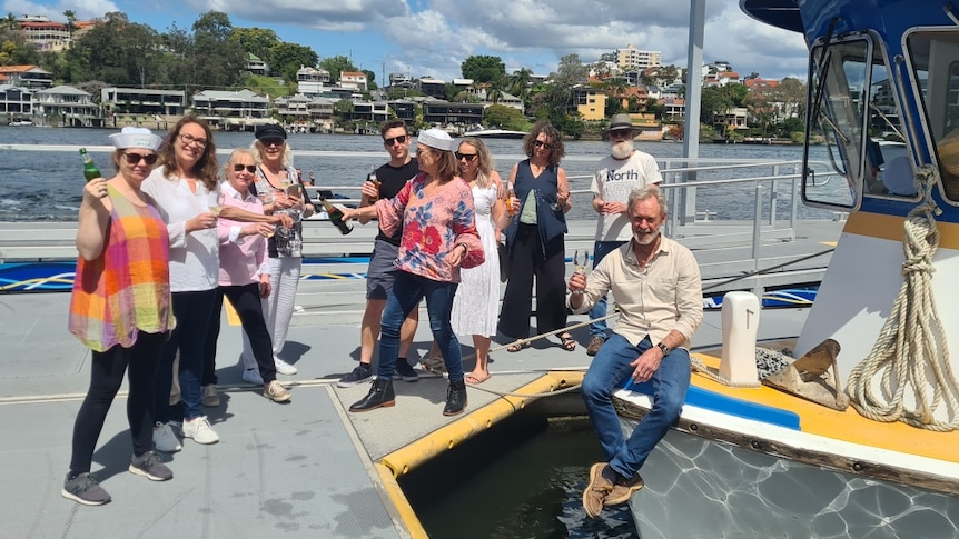 Man sitting on bow of ferry, friends on dock with champagne