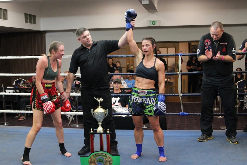 A woman's arm is raised by a referee in a boxing ring at the end of a fight.