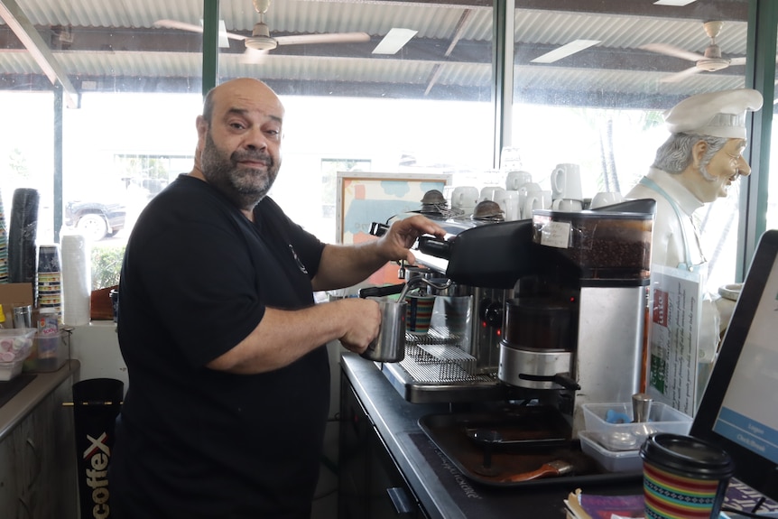 A man stands in front of a coffee machine inside a cafe.