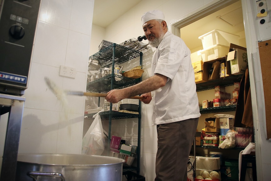 A chef cooks a meal in a pot in a commercial kitchen.
