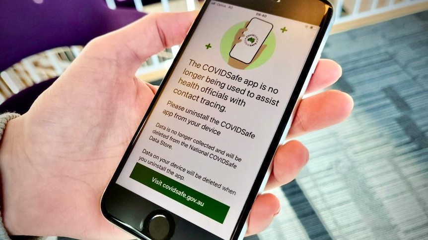 a hand holds a screen showing the message on the covidsafe app that it will no longer be collecting data