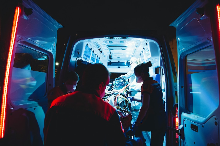 looking into the back of an ambulance, with paramedics surrouding a stretcher