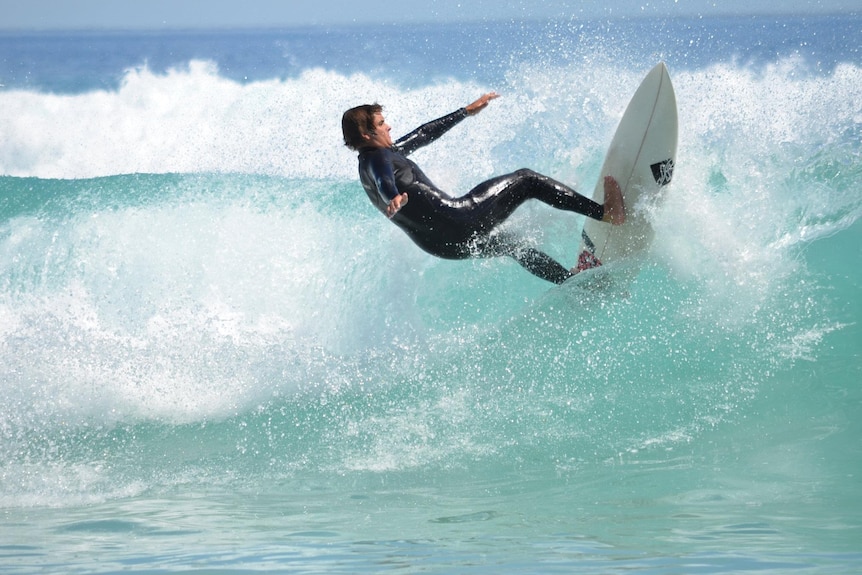A man surfs up a wave in clear aqua water.
