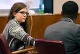 A woman sits at a courtroom table next to her lawyer.