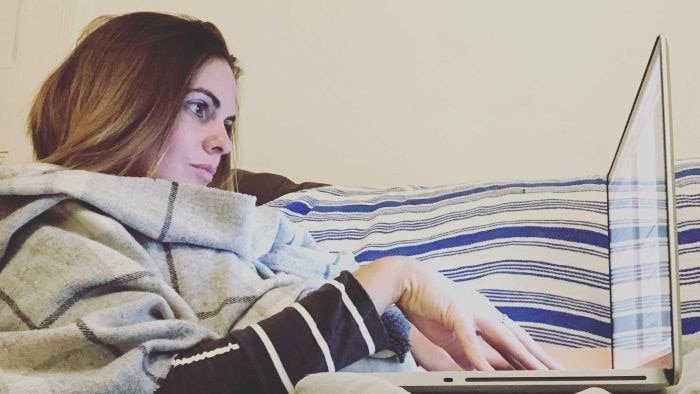 Writer Stephanie Coombes lying on her couch, typing on her laptop.
