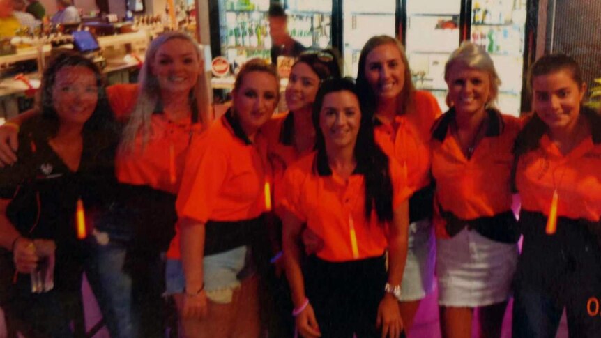 Group of smiling women in high vis uniforms at a bar.