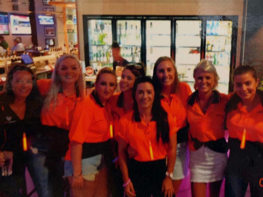 Group of smiling women in high vis uniforms at a bar.