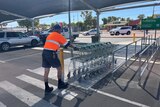 A man in a day glow shirt pushing trolleys in a car park  