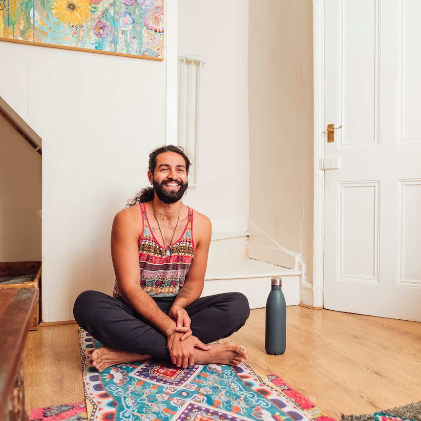 young man smiling sitting cross legged on colourful yoga mat